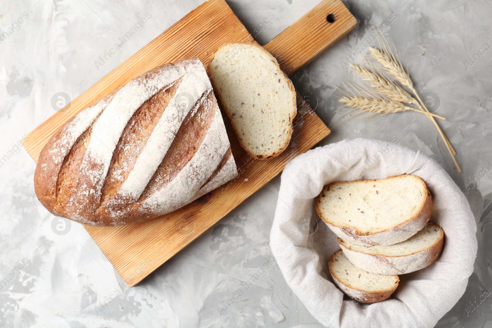 Photo of Wooden cutting board with fresh bread and spikes on grey table, flat lay