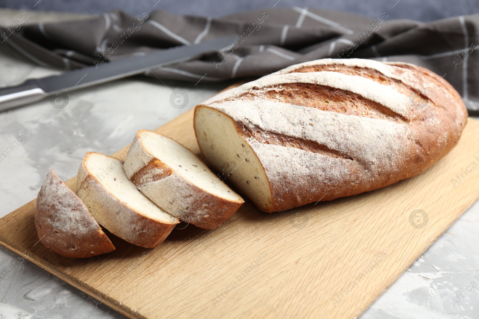 Photo of Wooden cutting board with fresh bread and knife on grey table, closeup