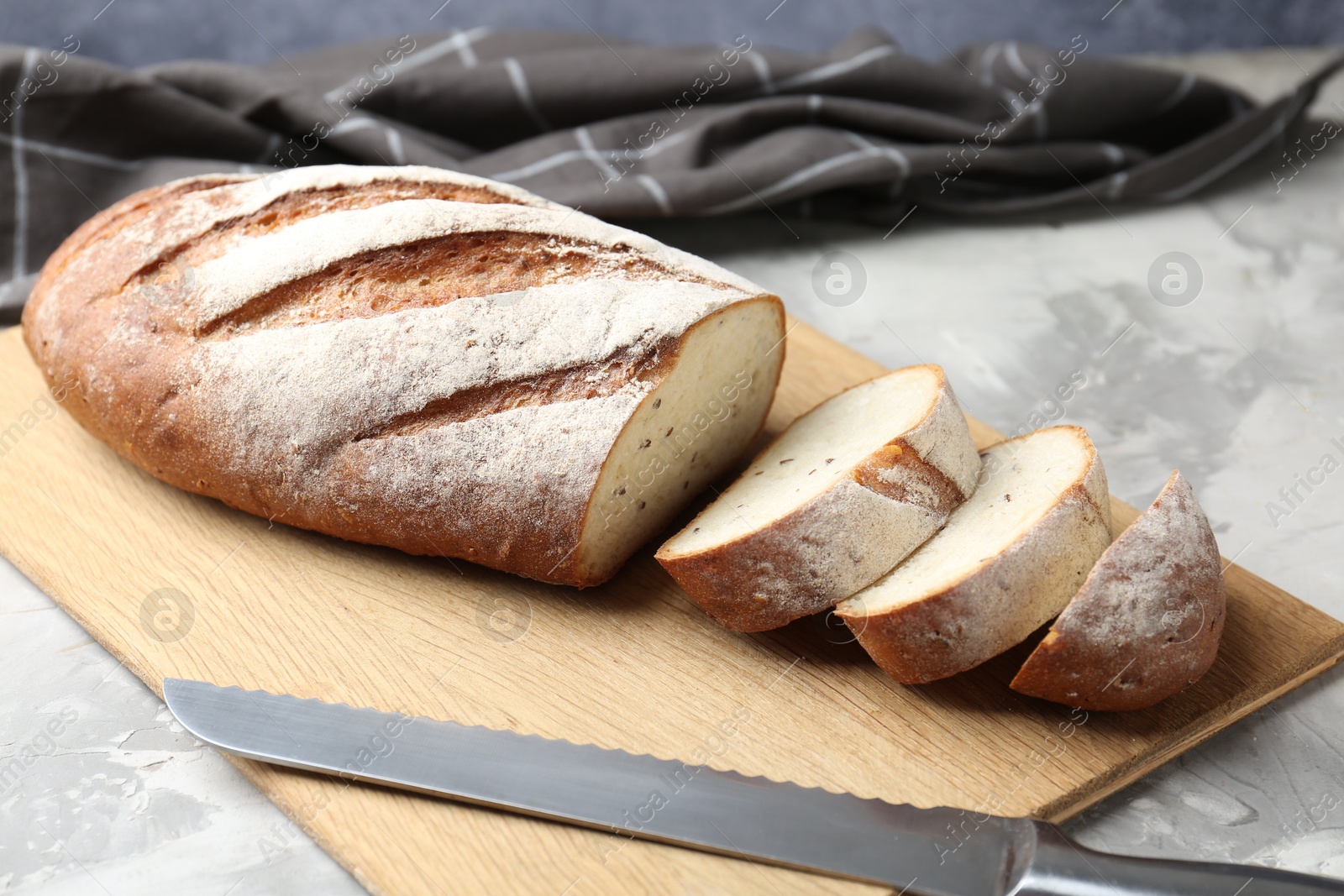 Photo of Wooden cutting board with fresh bread and knife on grey table, closeup