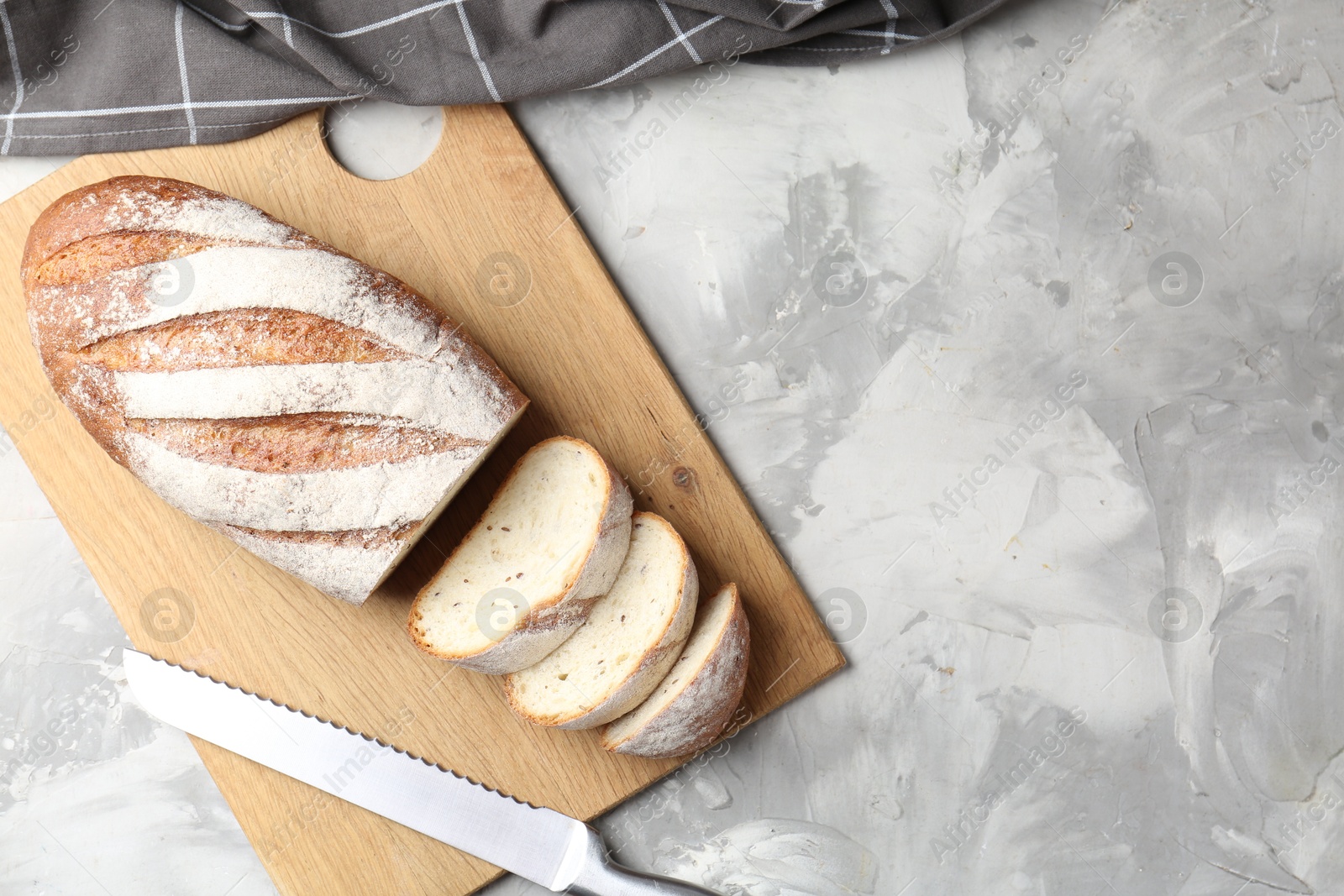 Photo of Wooden cutting board with fresh bread and knife on grey table, top view. Space for text