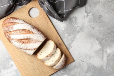 Photo of Wooden cutting board with fresh bread and knife on grey table, top view. Space for text