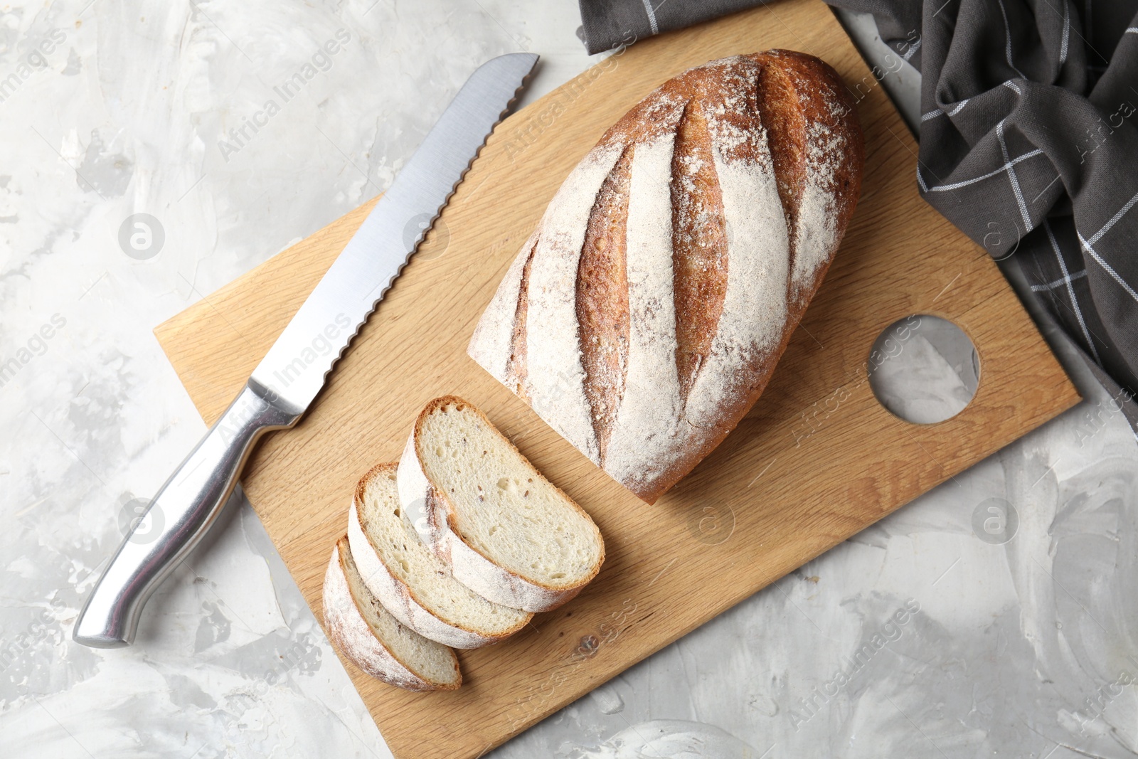 Photo of Wooden cutting board with fresh bread and knife on grey table, top view