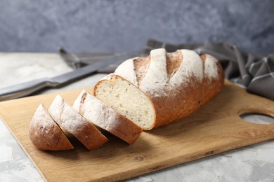 Photo of Wooden cutting board with fresh bread and knife on grey table, closeup