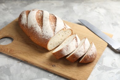 Photo of Wooden cutting board with fresh bread and knife on grey table, closeup