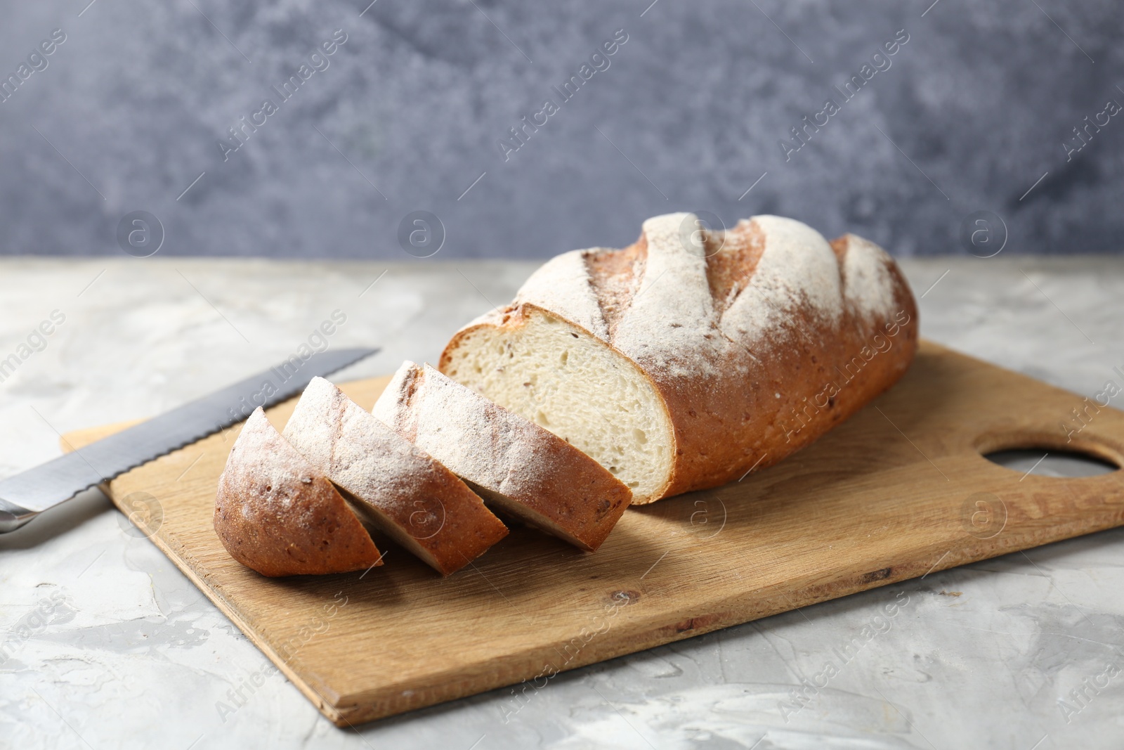 Photo of Wooden cutting board with fresh bread and knife on grey table, closeup