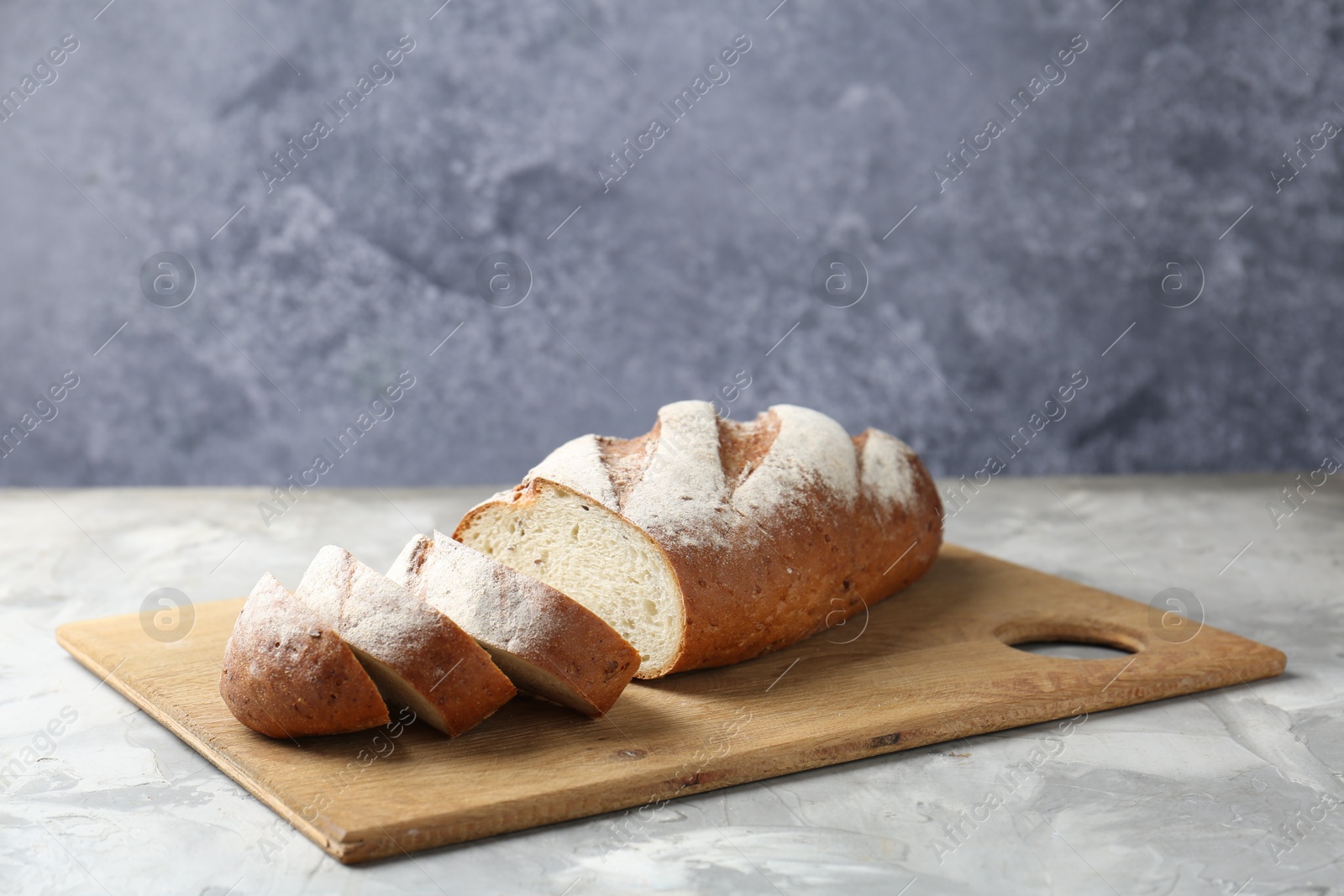 Photo of Wooden cutting board with fresh bread on grey table, closeup