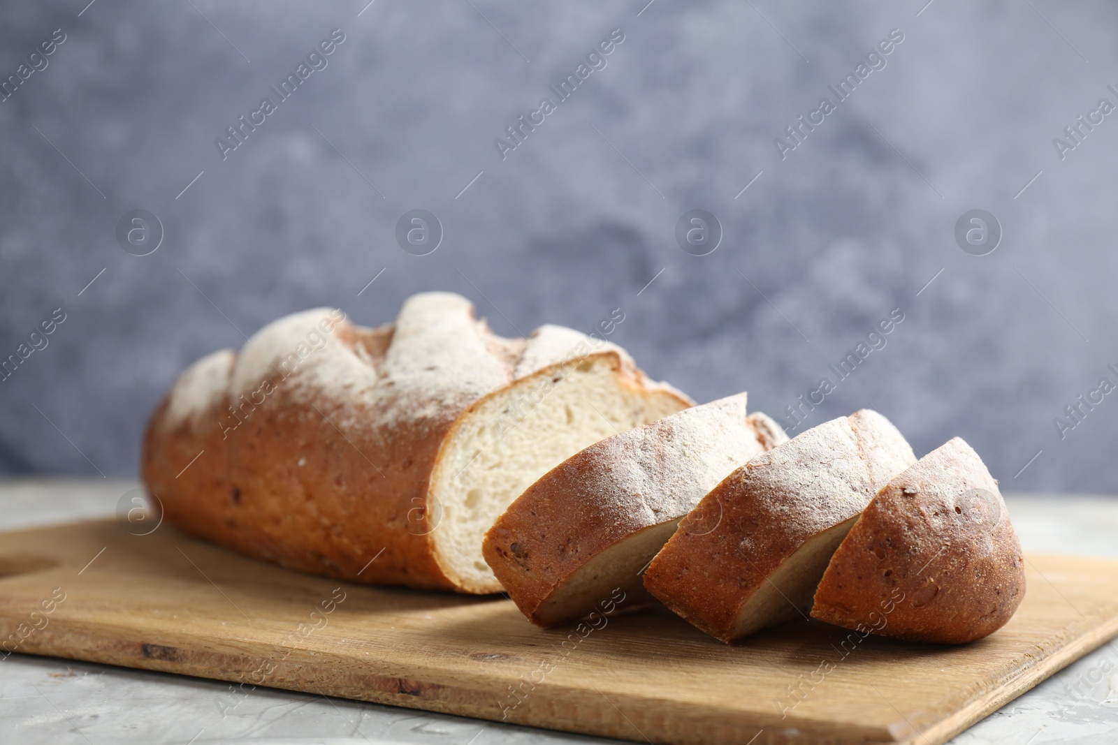 Photo of Wooden cutting board with fresh bread on grey table, closeup