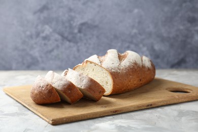 Photo of Wooden cutting board with fresh bread on grey table, closeup