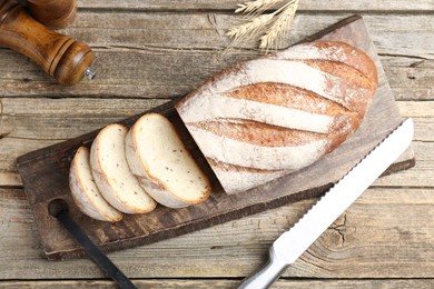 Photo of Cutting board with fresh bread, knife, spikes and shakers on wooden table, flat lay