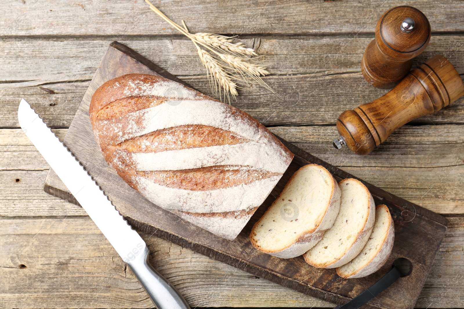 Photo of Cutting board with fresh bread, knife, spikes and shakers on wooden table, flat lay