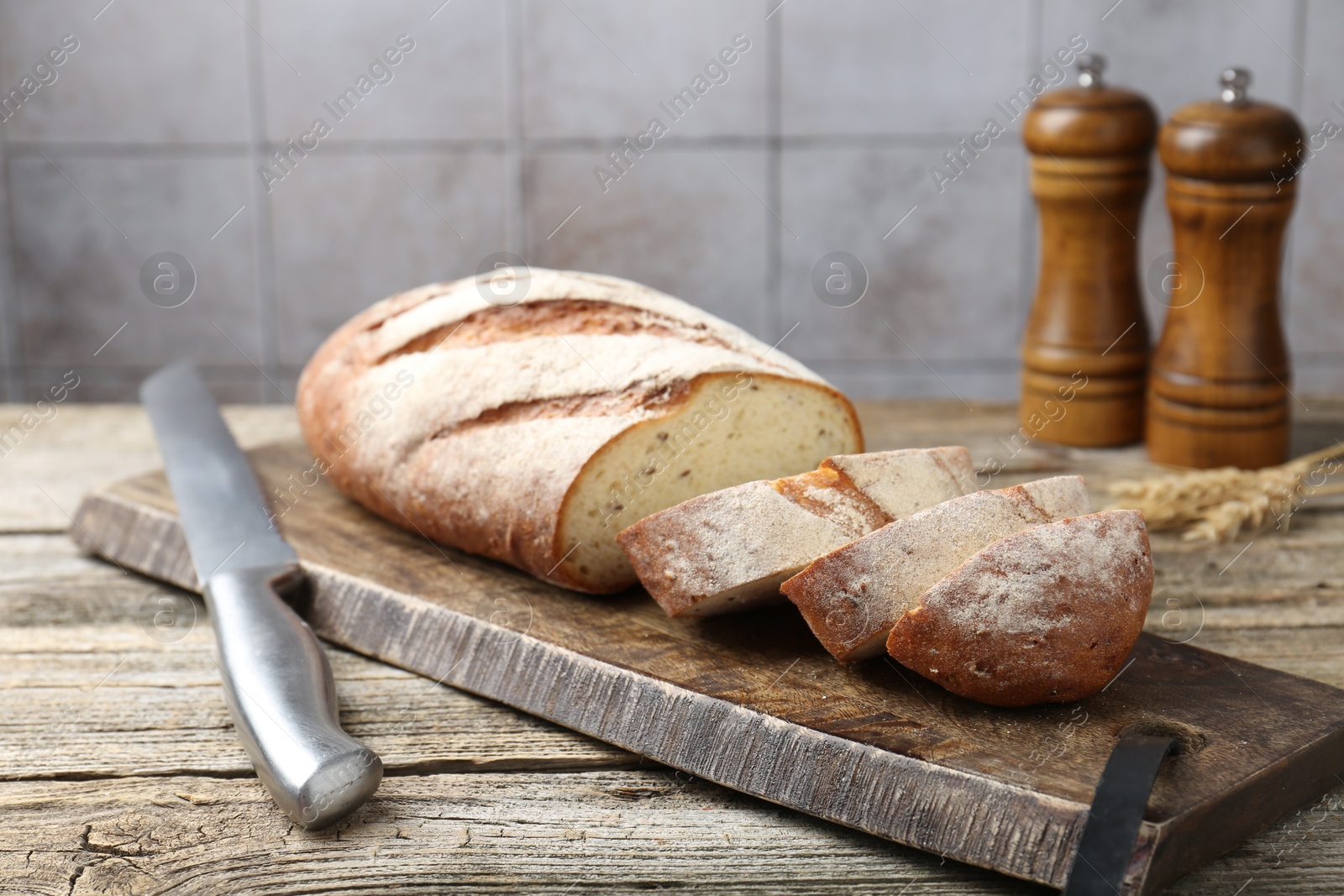 Photo of Cutting board with fresh bread, knife, spikes and shakers on wooden table, closeup