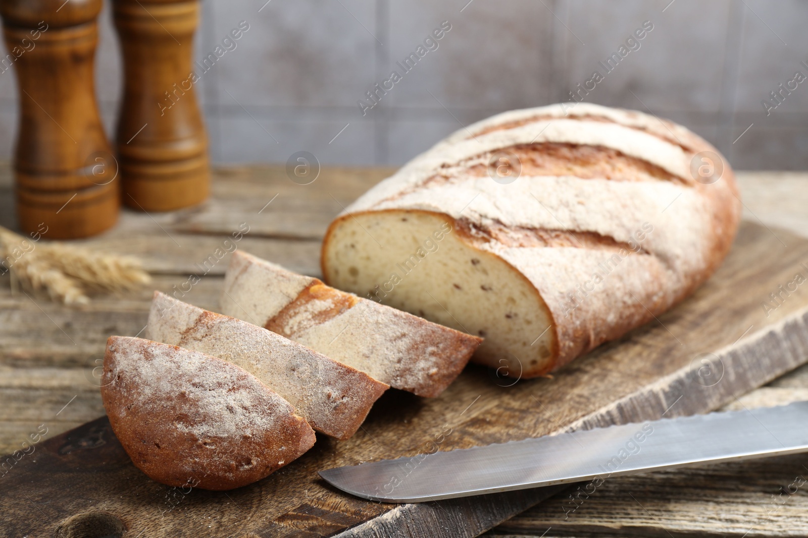 Photo of Cutting board with fresh bread, knife, spikes and shakers on wooden table, closeup