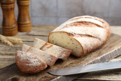 Photo of Cutting board with fresh bread, knife, spikes and shakers on wooden table, closeup