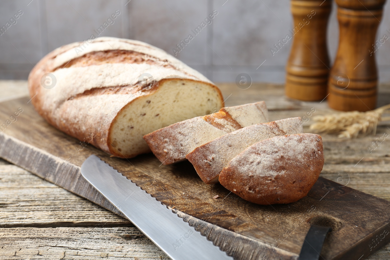 Photo of Cutting board with fresh bread, knife, spikes and shakers on wooden table, closeup