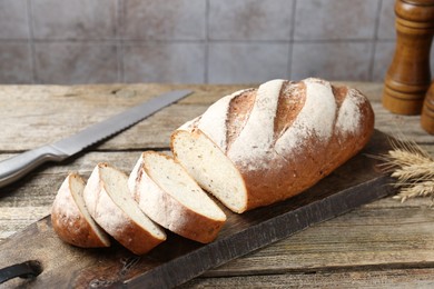 Photo of Cutting board with fresh bread, knife, spikes and shakers on wooden table, closeup