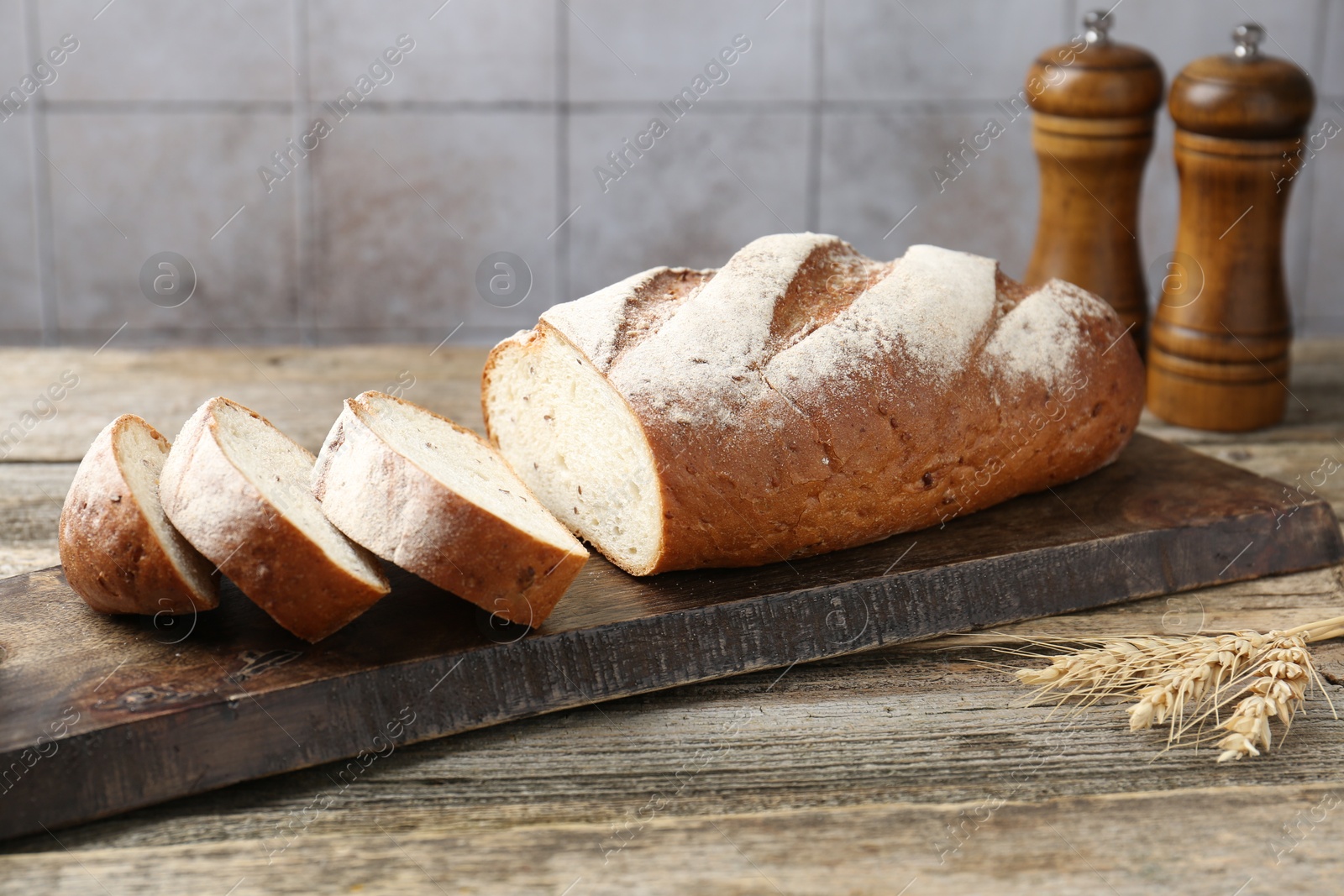 Photo of Cutting board with fresh bread, spikes and shakers on wooden table, closeup