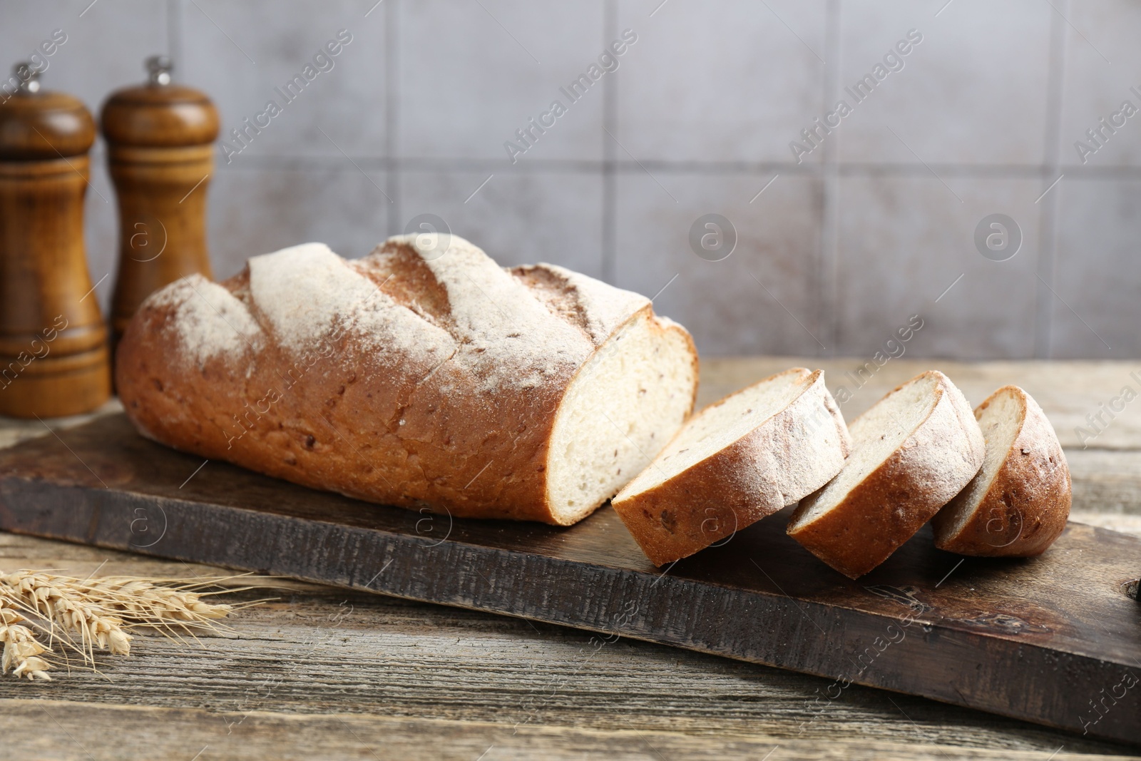 Photo of Cutting board with fresh bread, spikes and shakers on wooden table, closeup