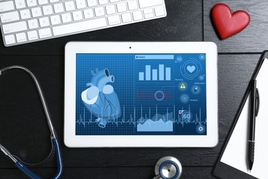 Image of Cardiology. Doctor's workplace with stethoscope and tablet computer on black wooden table, top view. Data on device screen