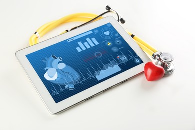 Image of Cardiology. Tablet computer with data, red heart and stethoscope on white table