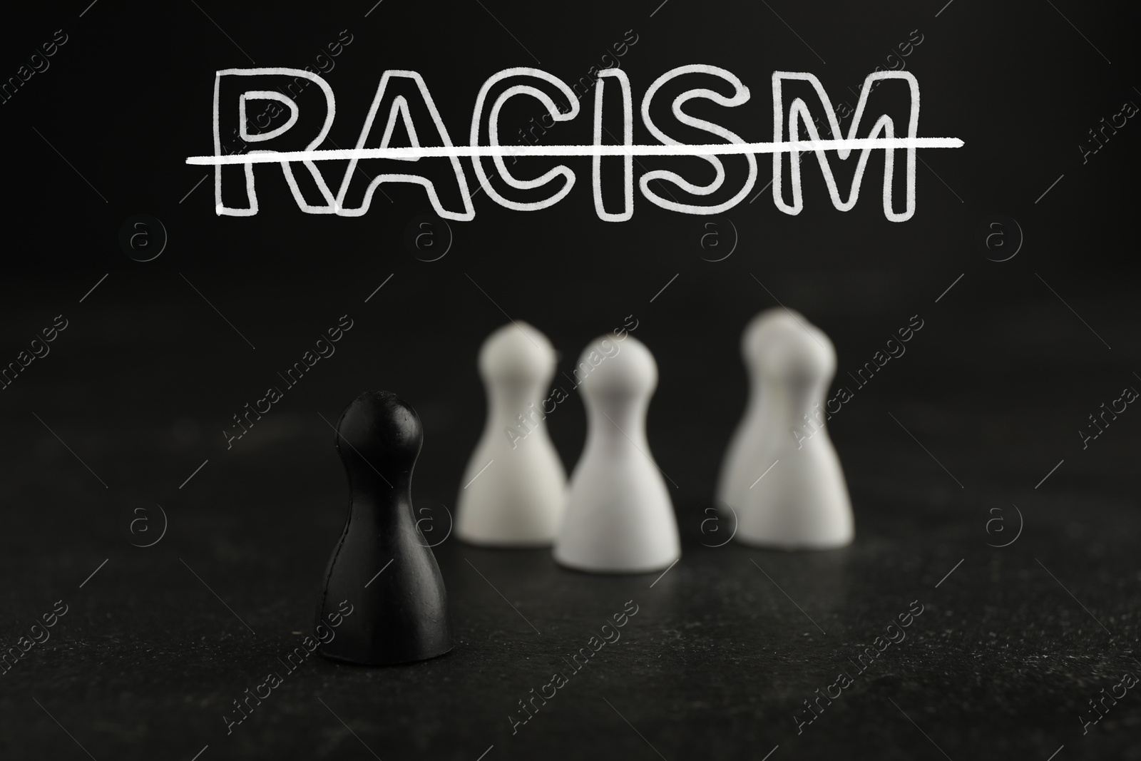 Image of Stop racism. Black game piece standing apart from white ones on table. Strikethrough word