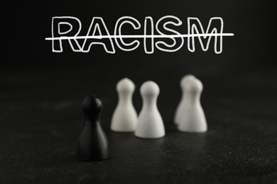 Image of Stop racism. Black game piece standing apart from white ones on table. Strikethrough word