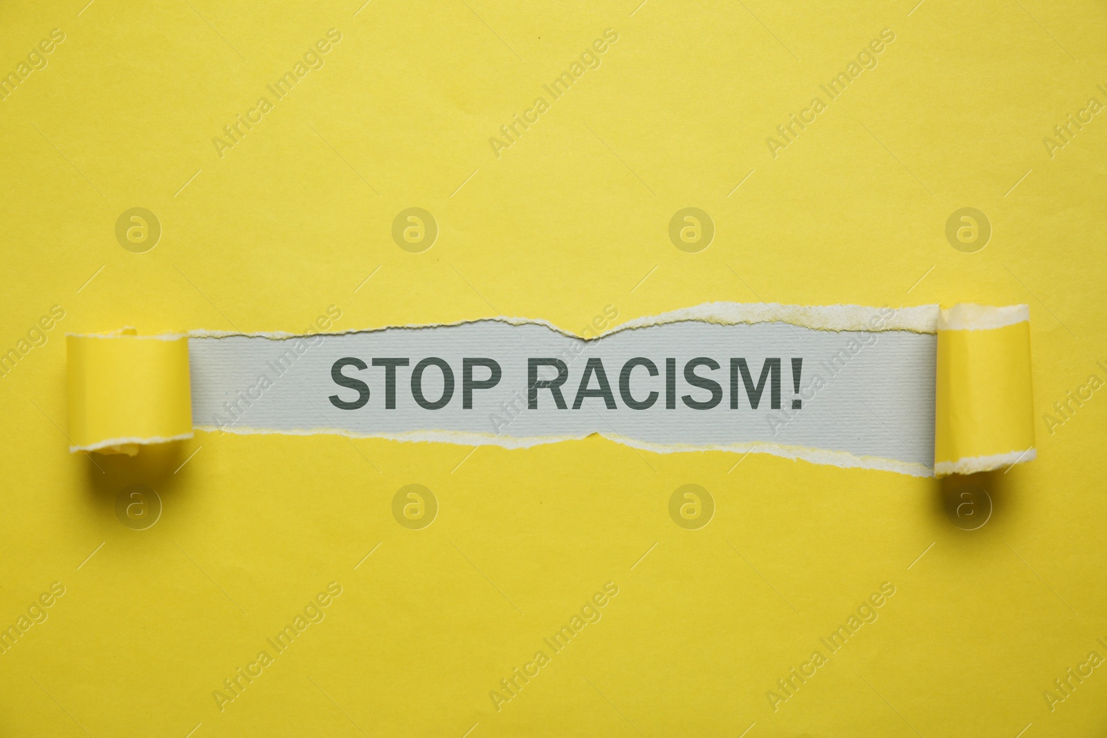 Image of Stop racism. View on text through torn yellow paper