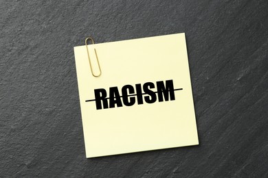 Image of Stop racism concept. Note with strikethrough word on dark grey textured background, top view