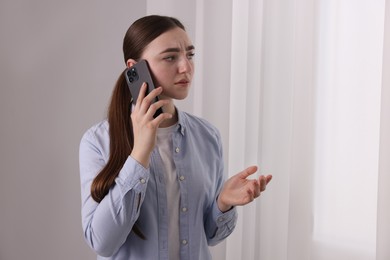 Photo of Stressed woman calling hotline for mental health help near window at home