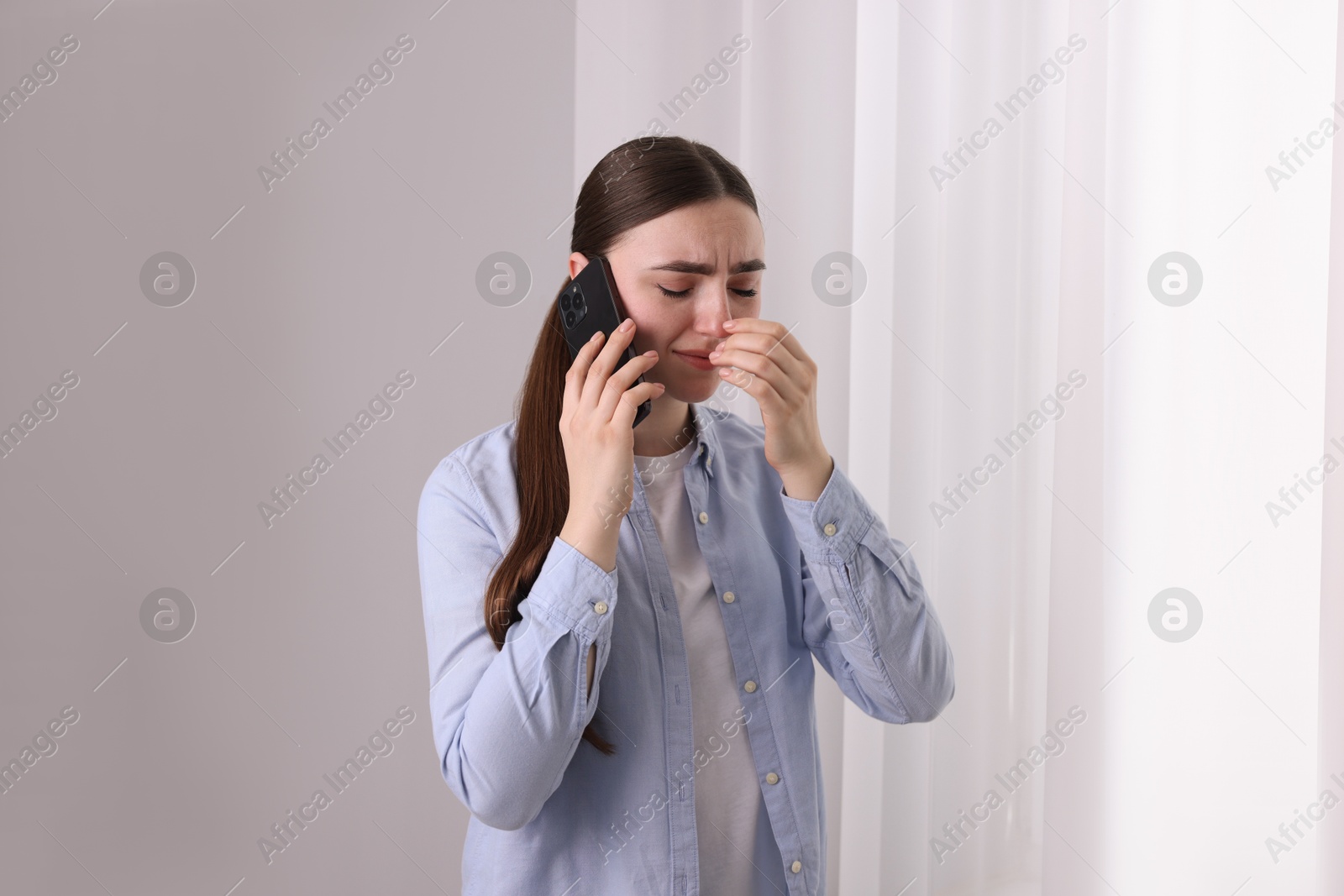 Photo of Stressed woman calling hotline for mental health help near window at home