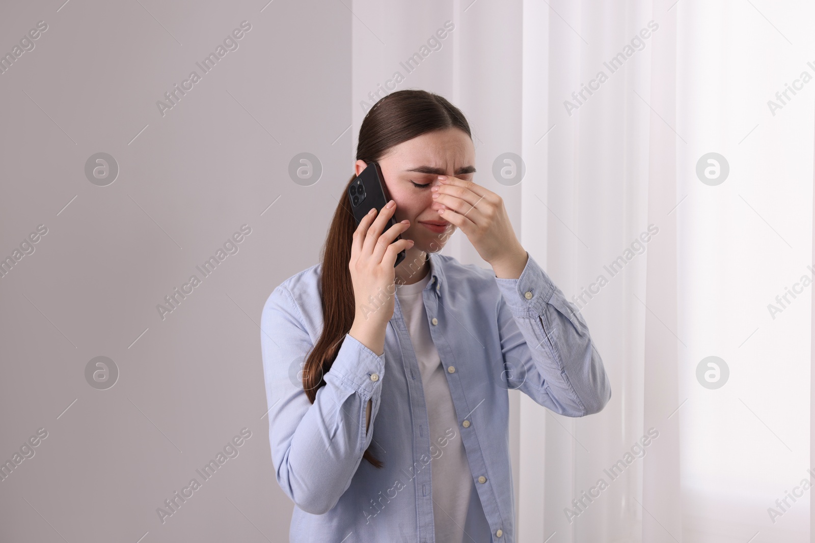 Photo of Stressed woman calling hotline for mental health help near window at home