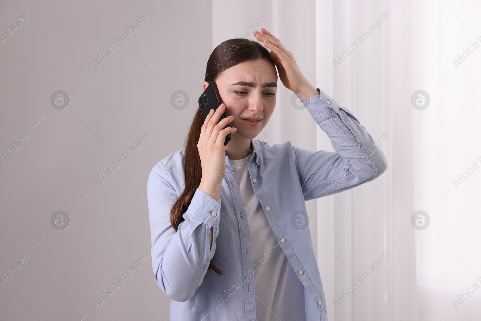 Photo of Stressed woman calling hotline for mental health help near window at home