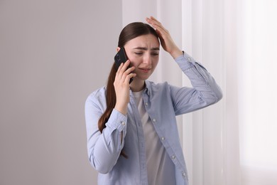 Photo of Stressed woman calling hotline for mental health help near window at home