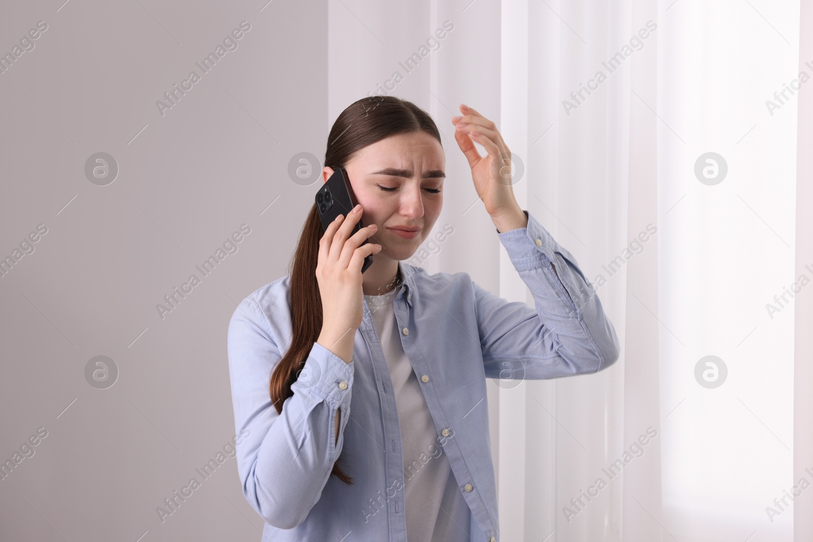 Photo of Stressed woman calling hotline for mental health help near window at home