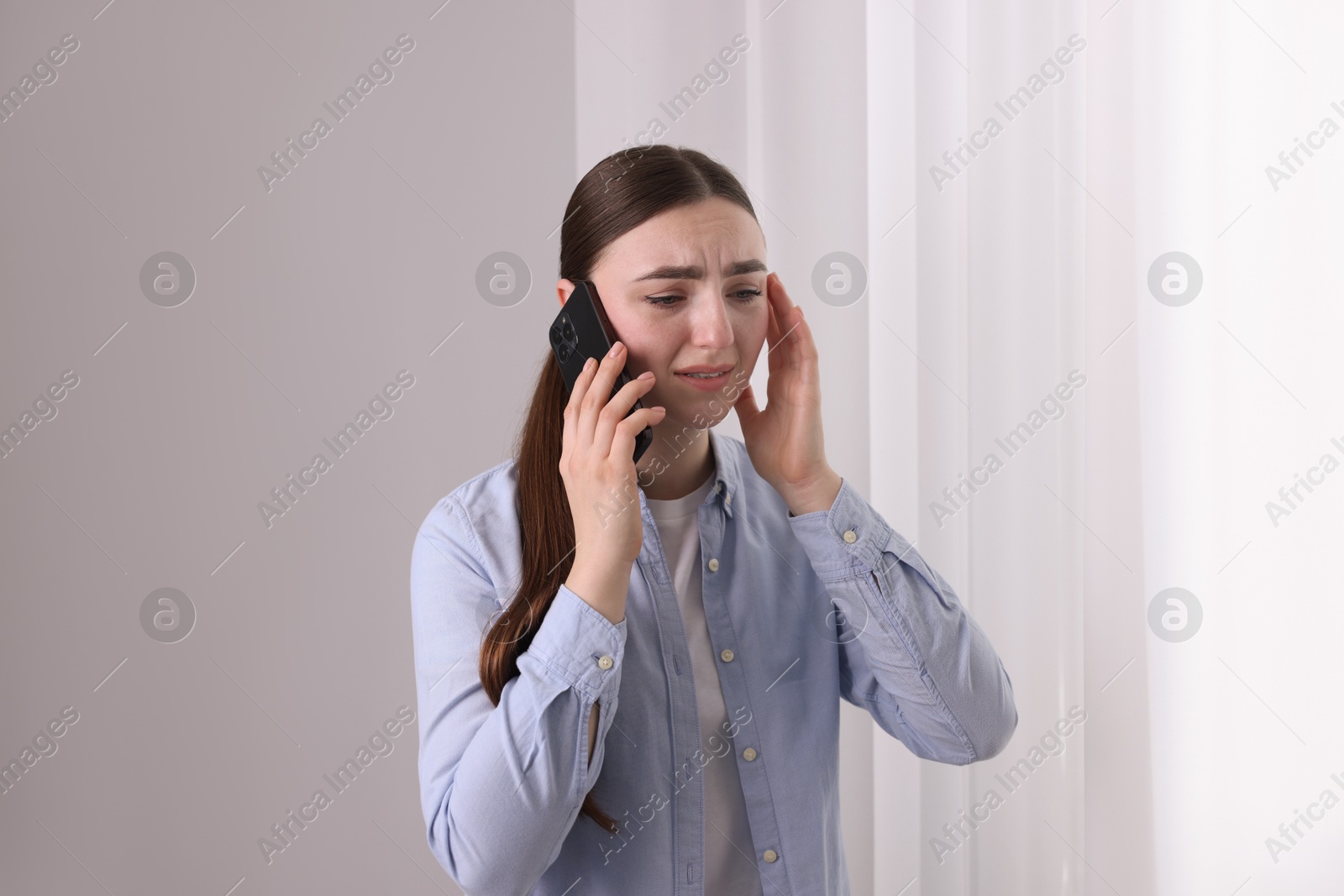 Photo of Stressed woman calling hotline for mental health help near window at home