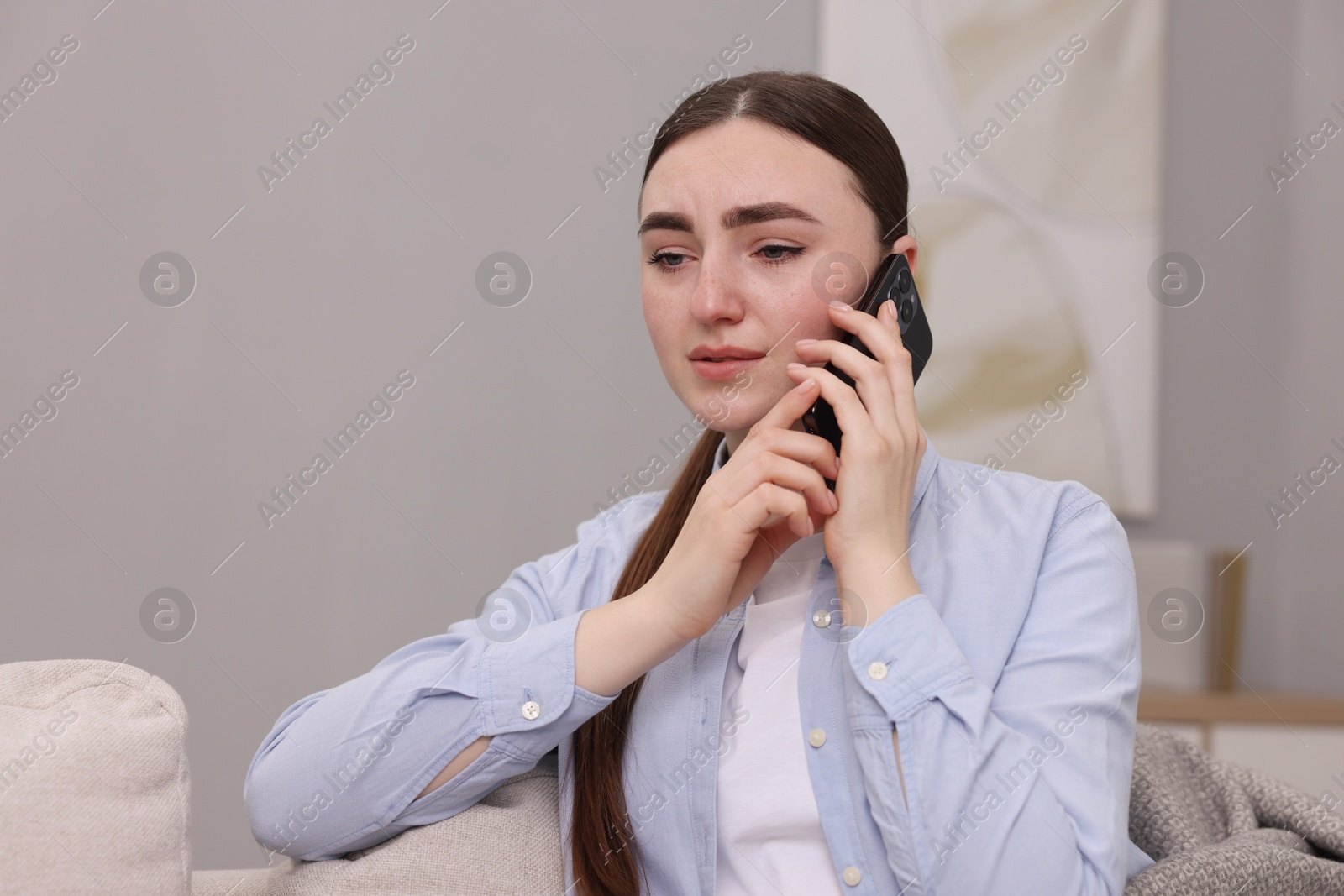 Photo of Depressed woman calling hotline for mental health help on sofa at home. Space for text