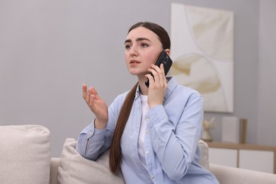 Photo of Depressed woman calling hotline for mental health help on sofa at home