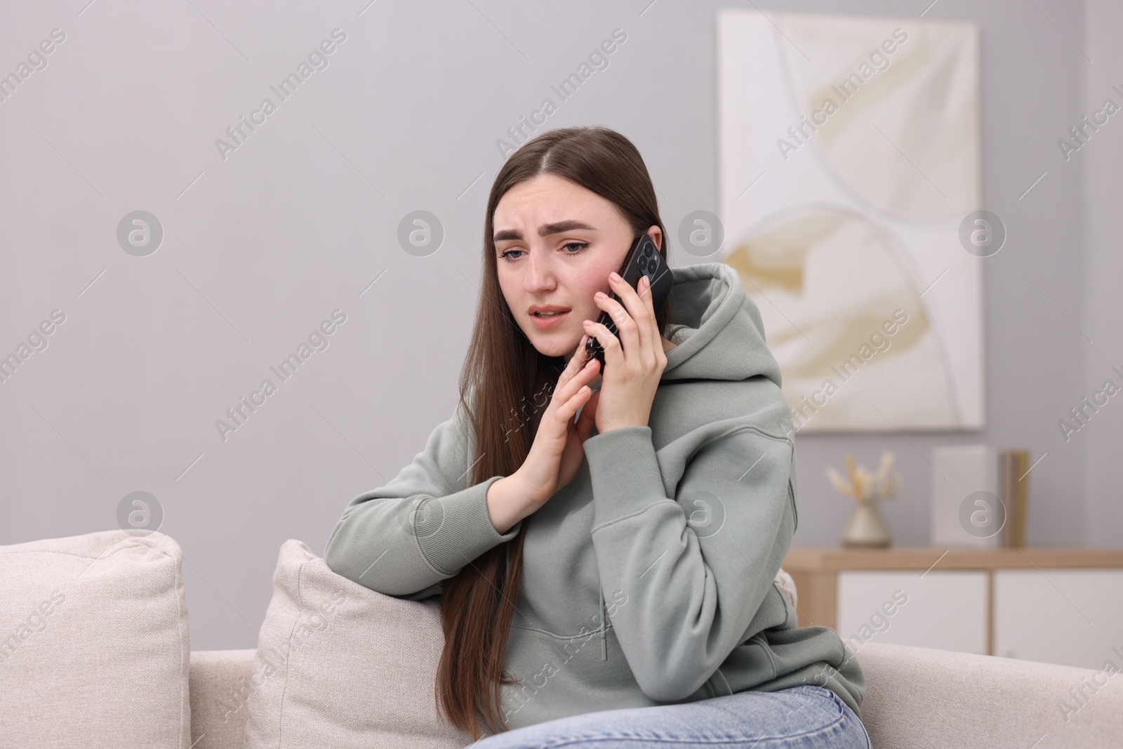 Photo of Depressed woman calling hotline for mental health help on sofa at home