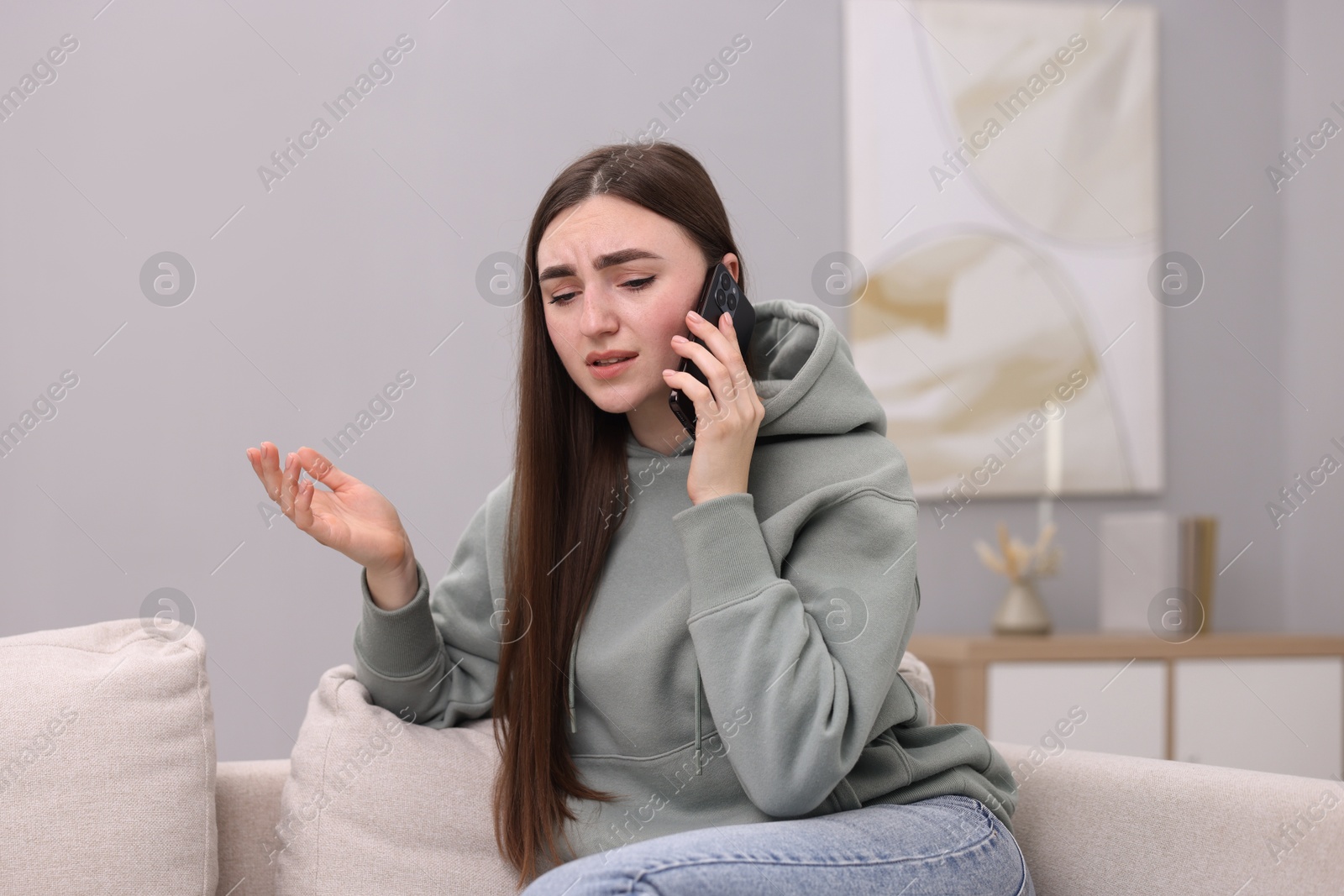 Photo of Depressed woman calling hotline for mental health help on sofa at home