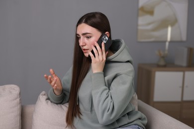 Depressed woman calling hotline for mental health help on sofa at home