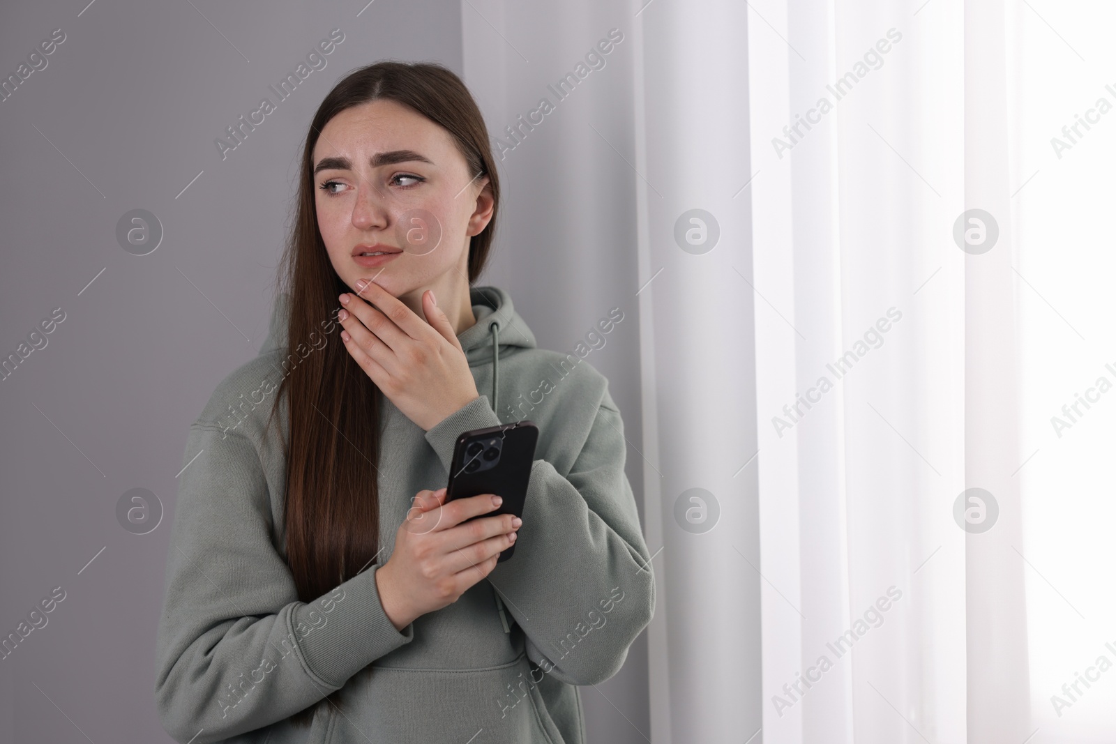 Photo of Desperate woman calling hotline for mental health help near window at home. Space for text