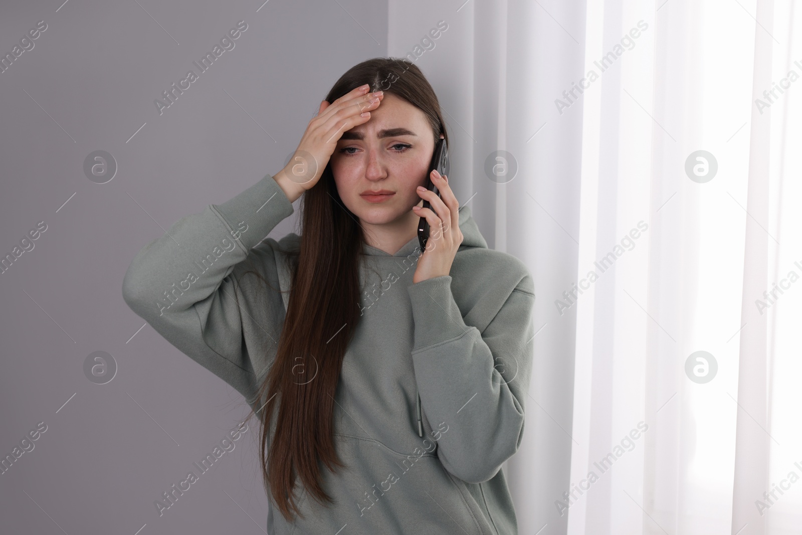 Photo of Desperate woman calling hotline for mental health help near window at home