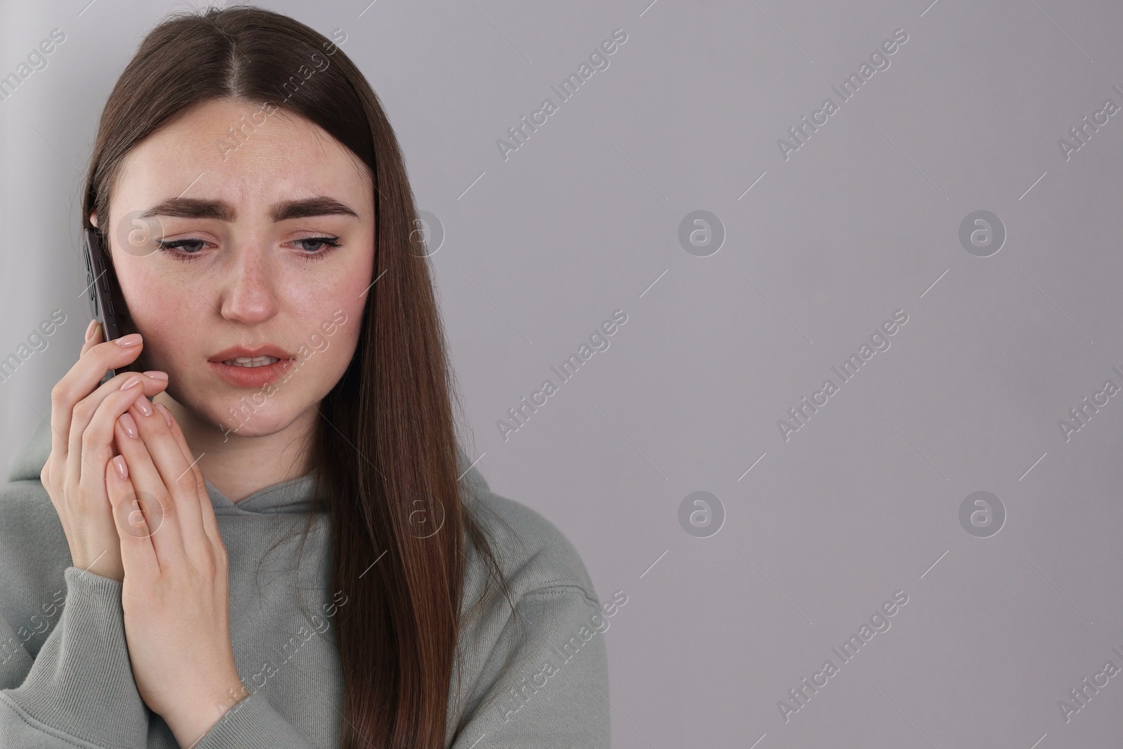 Photo of Stressed woman calling hotline for mental health help on grey background. Space for text