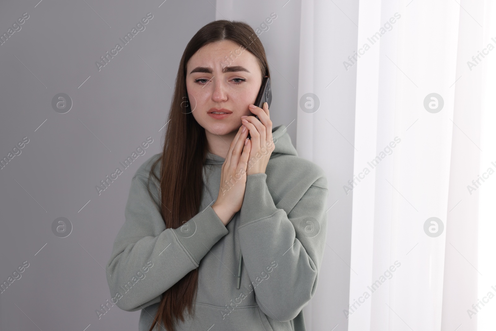 Photo of Desperate woman calling hotline for mental health help near window at home