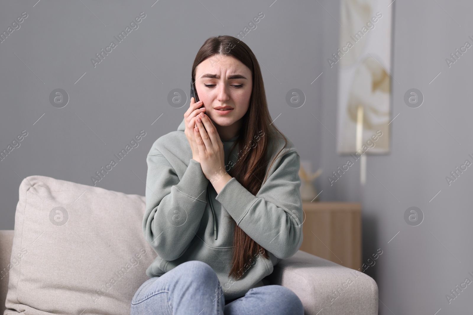 Photo of Depressed woman calling hotline for mental health help on sofa at home