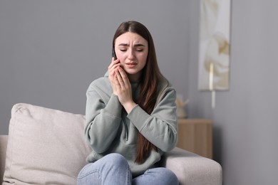 Photo of Depressed woman calling hotline for mental health help on sofa at home