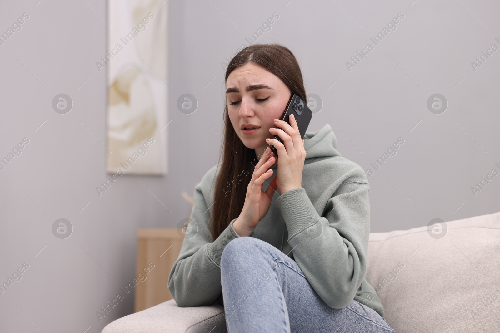 Photo of Depressed woman calling hotline for mental health help on sofa at home