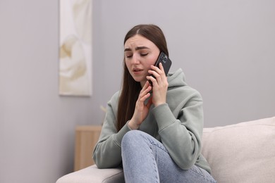 Photo of Depressed woman calling hotline for mental health help on sofa at home