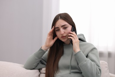 Photo of Depressed woman calling hotline for mental health help on sofa at home