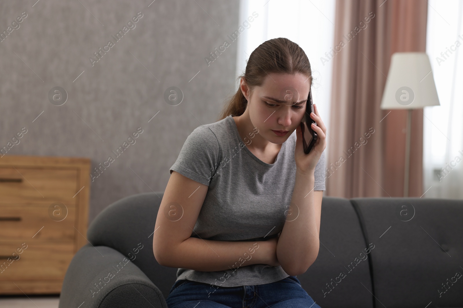 Photo of Depressed woman calling hotline for mental health help on sofa at home