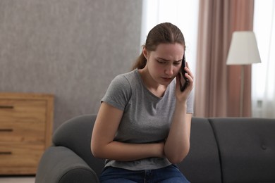 Photo of Depressed woman calling hotline for mental health help on sofa at home